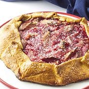 red rimmed white cake plate with baked rhubarb gallette sprinkled with large grain sugar crystals and a navy blue napkin in the background