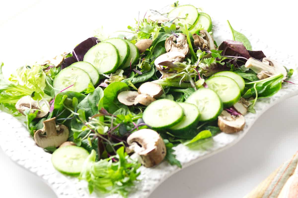 white platter with fresh lettuces, cucumber slices, mushrooms, and sprouts.