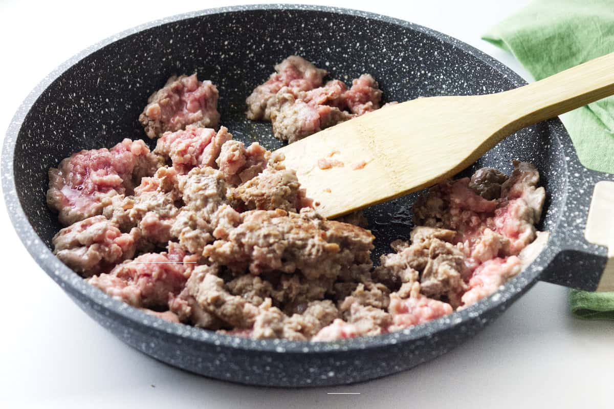 ground pork in a grey speckled skillet with a wooden spoon.