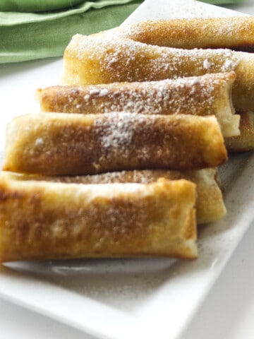 banana lumpia on a white platter with powdered sugar sprinkled on top