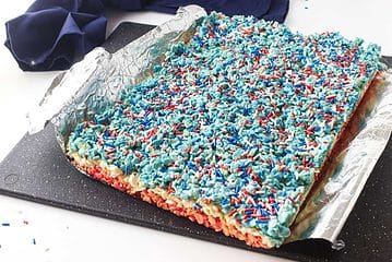 white tray with red, white, and blue layered rice crispy treats with sprinkles on top.