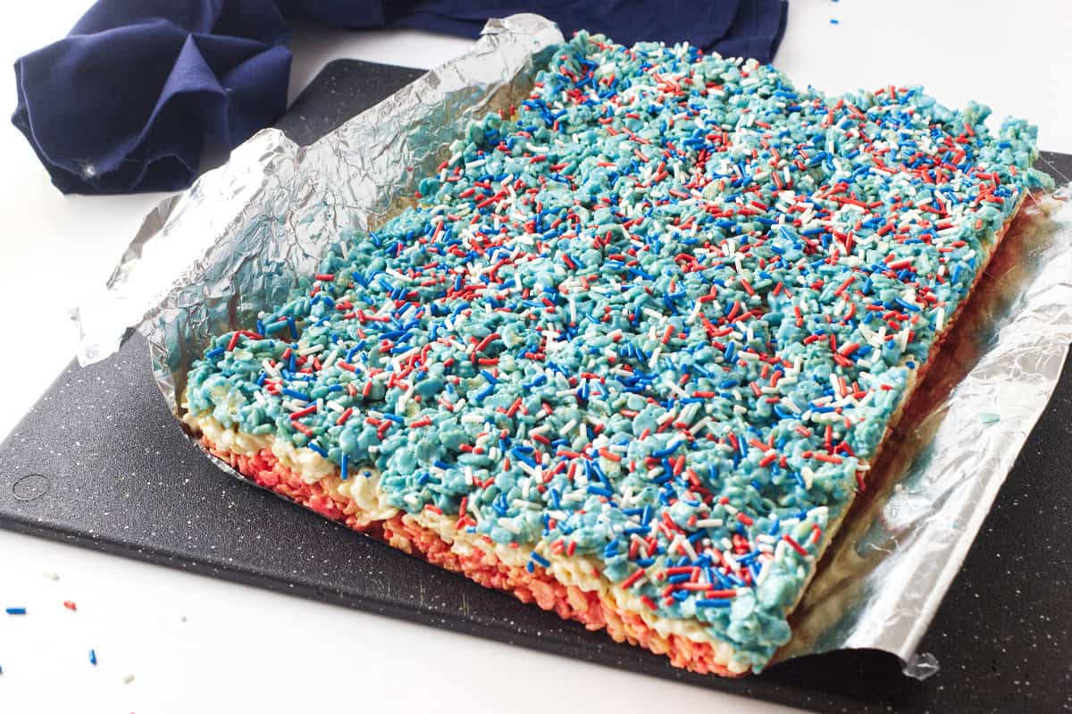 white tray with red, white, and blue layered rice crispy treats with sprinkles on top.