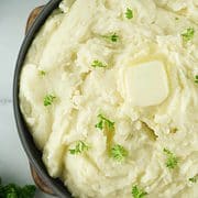 serving bowl of mashed potatoes garnished with butter & parsley.