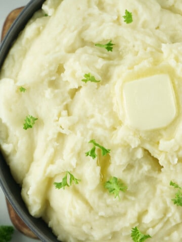 serving bowl of mashed potatoes garnished with butter & parsley.