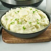 mashed potatoes in a bowl garnished with parsley and butter, with instant pot in background.