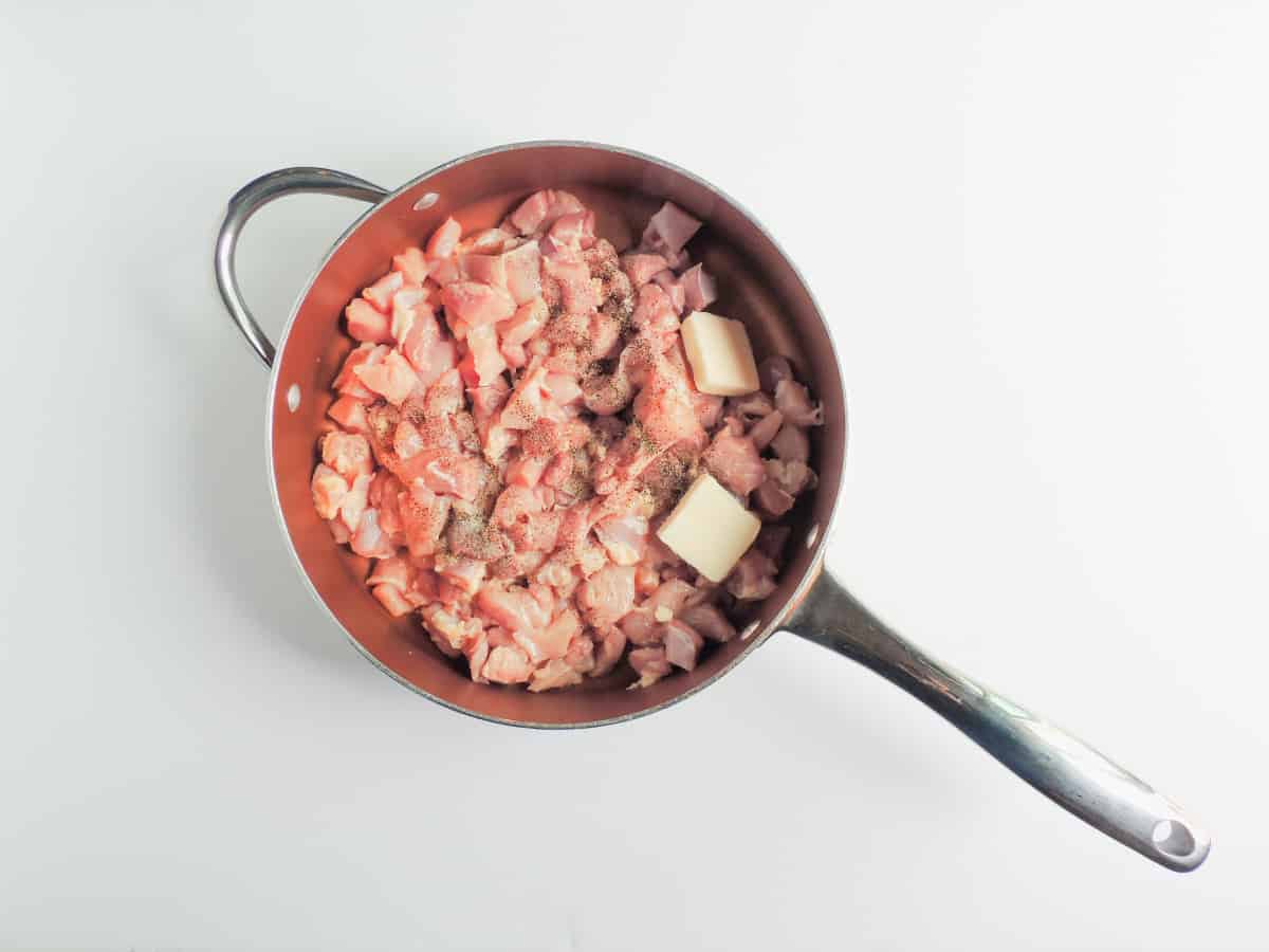 raw chopped up chicken in a skillet with some butter.