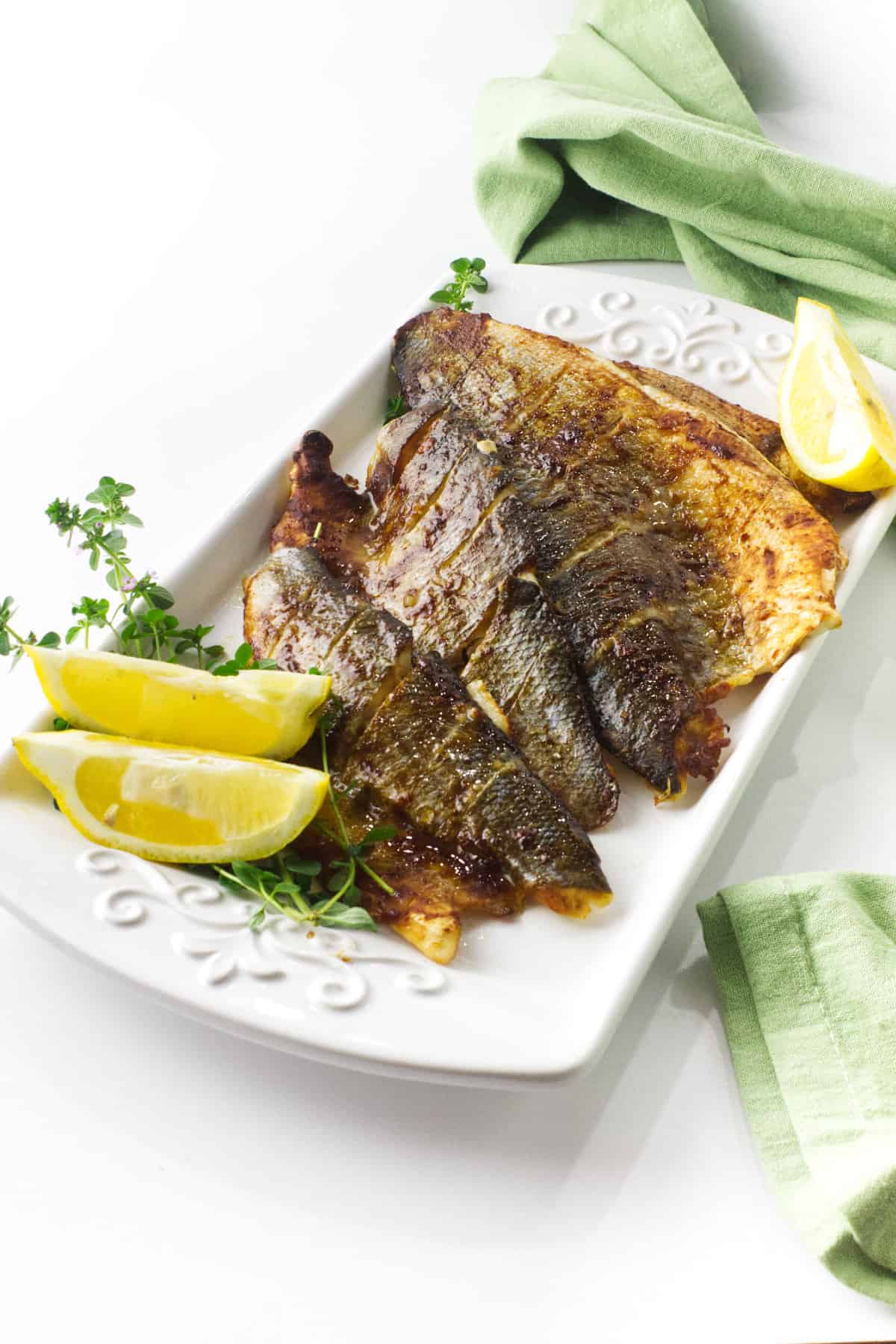 baked branzino glazed with miso sauce on a serving platter with lemon wedges.