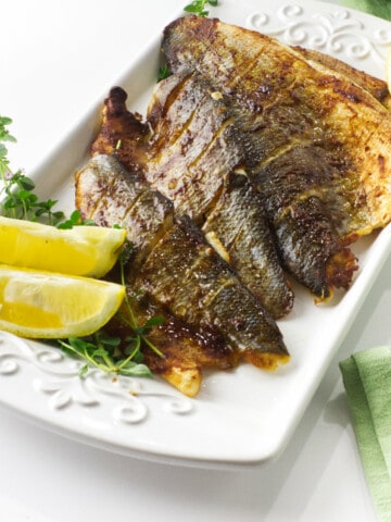 baked branzino glazed with miso sauce on a serving platter with lemon wedges.