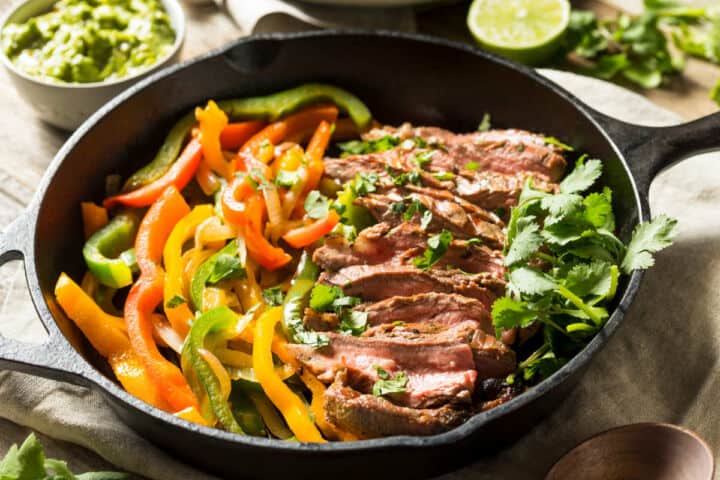 Chili's steak fajitas in a skillet: grilled steak, sautéed bell peppers, cilantro; guacamole and lime halves in the background.