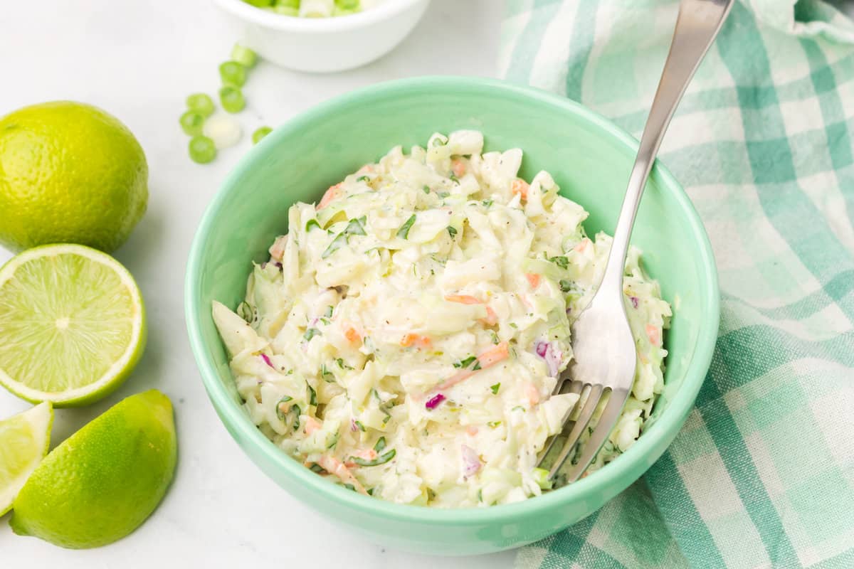 bowl of coleslaw with limes nearby.