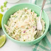 bowl of coleslaw with limes and green onions nearby..