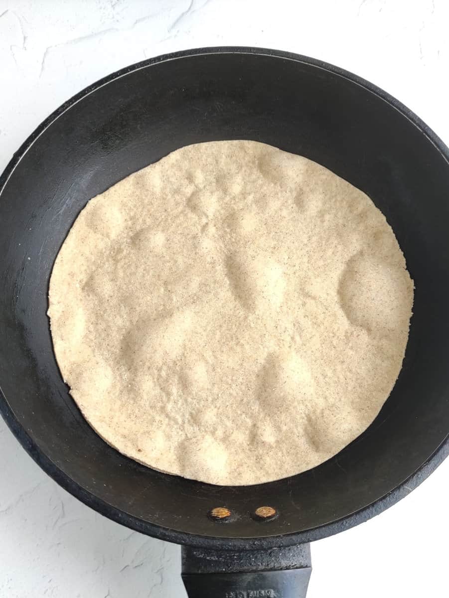 Tortilla placed in a skillet to cook one side.