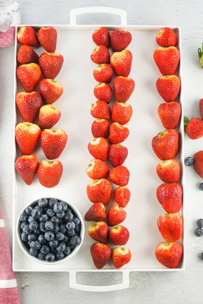 rows of strawberries and a bowl of blueberries on a regtangular white tray.