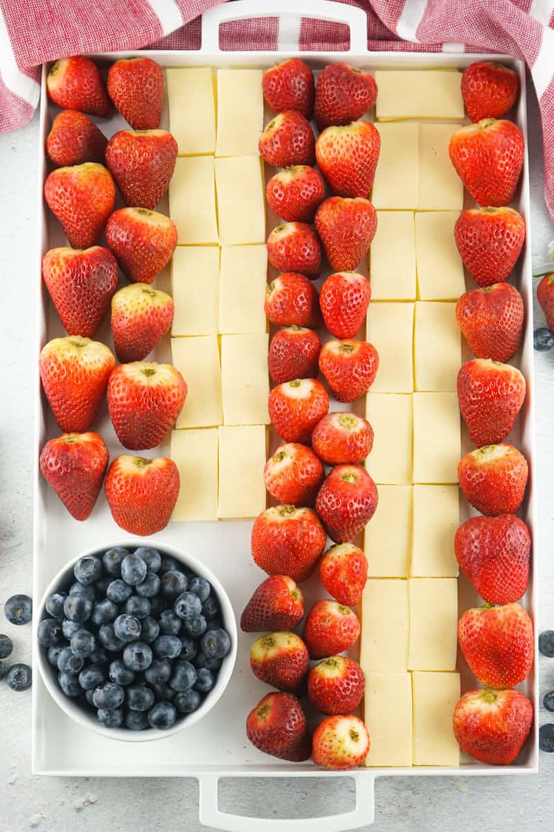 strawberries, white cheddar, and a bowl of blueberries on a white serving tray.