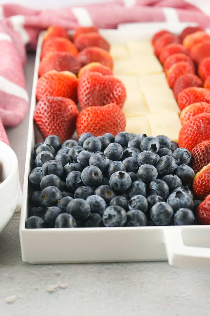 white plastic tray with blueberries and rows of white cheese and red strawberries.