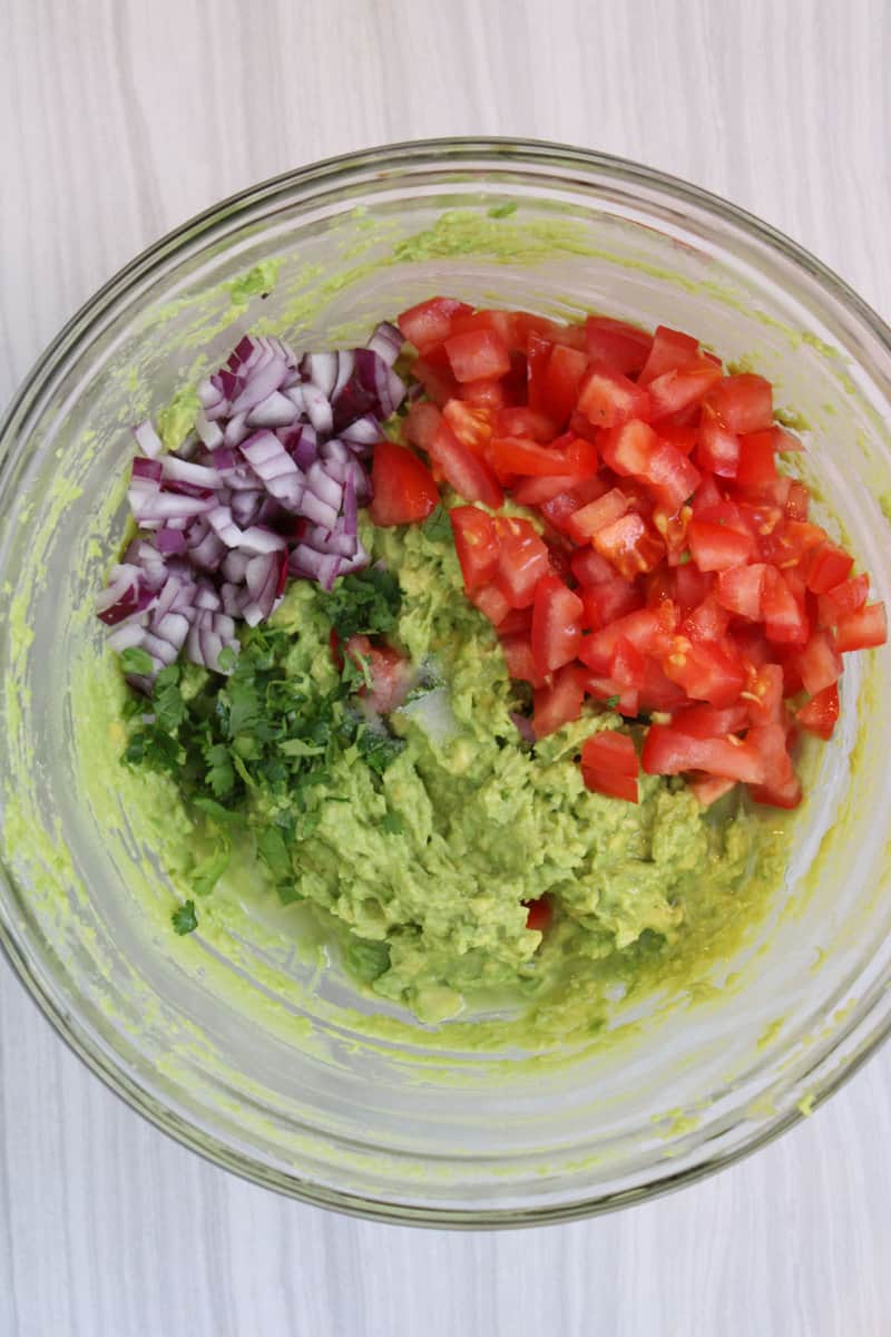 mashed avocados with piles of chopped onion, tomato, and cilantro.