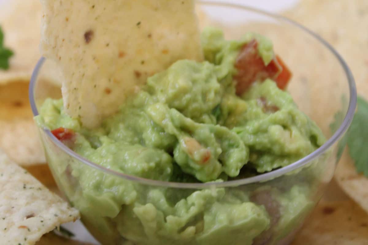 bowl of guacamole with tortilla chips on the side.