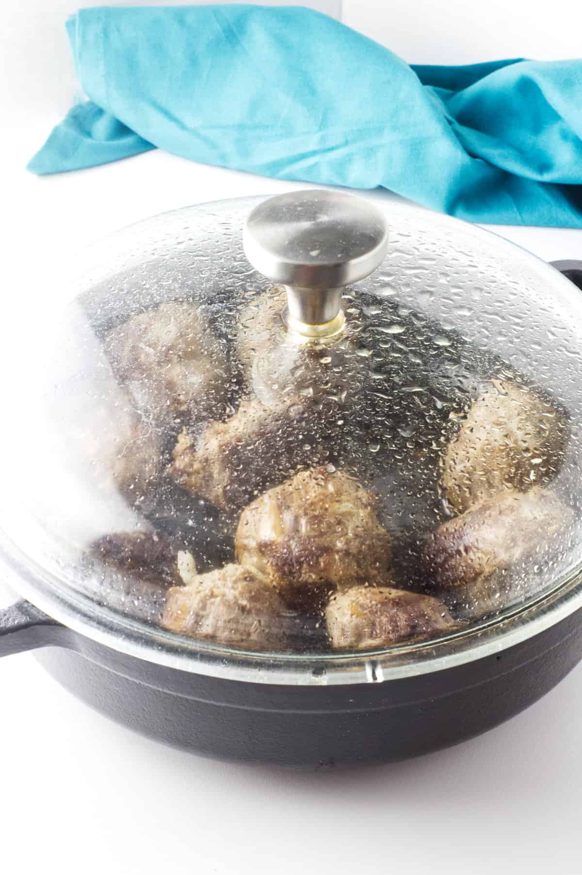 clear lid covered skillet of lamb kofta balls cooking on how heat.