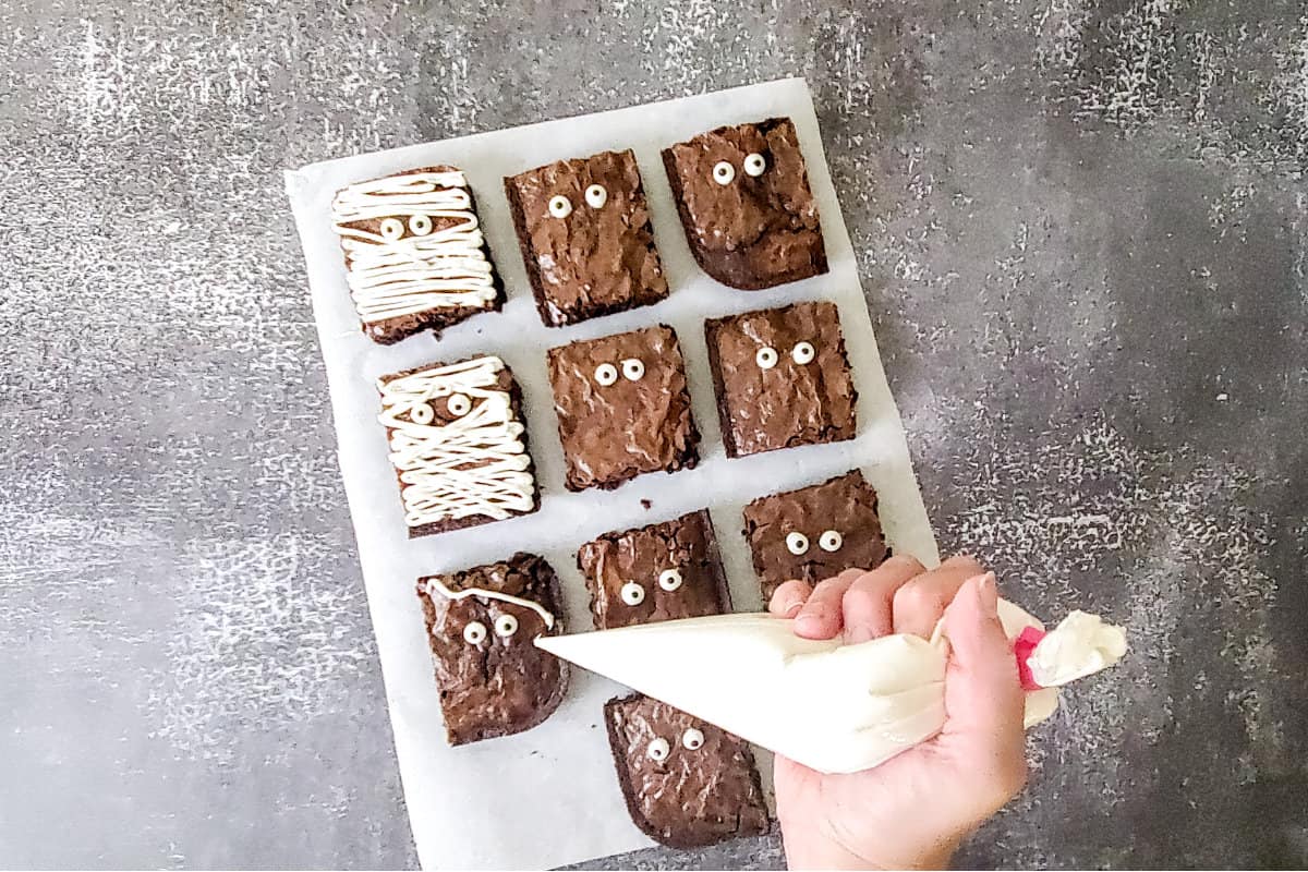 piping frosting on brownies to look like mummy wraps.