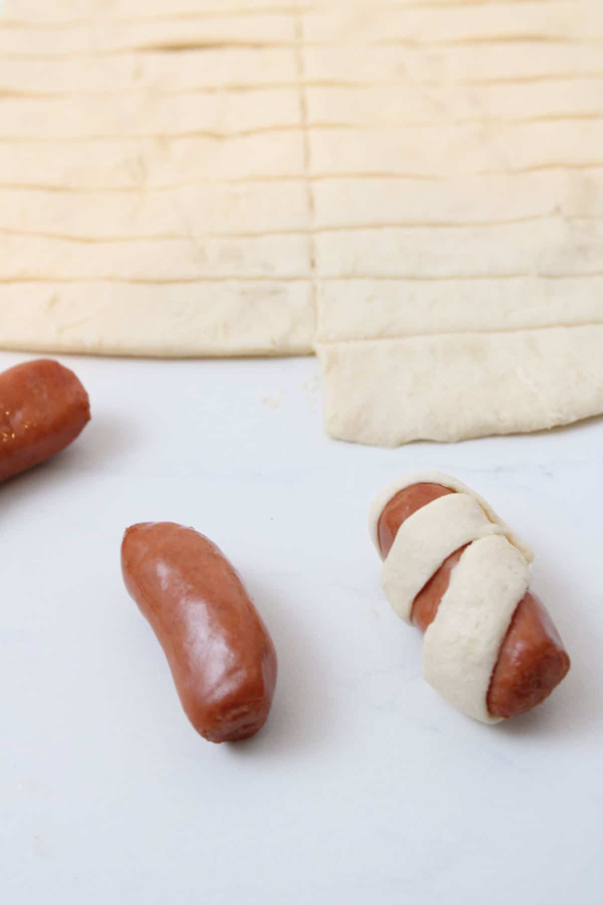 wrapping mini hot dogs in strips of crescent roll dough.