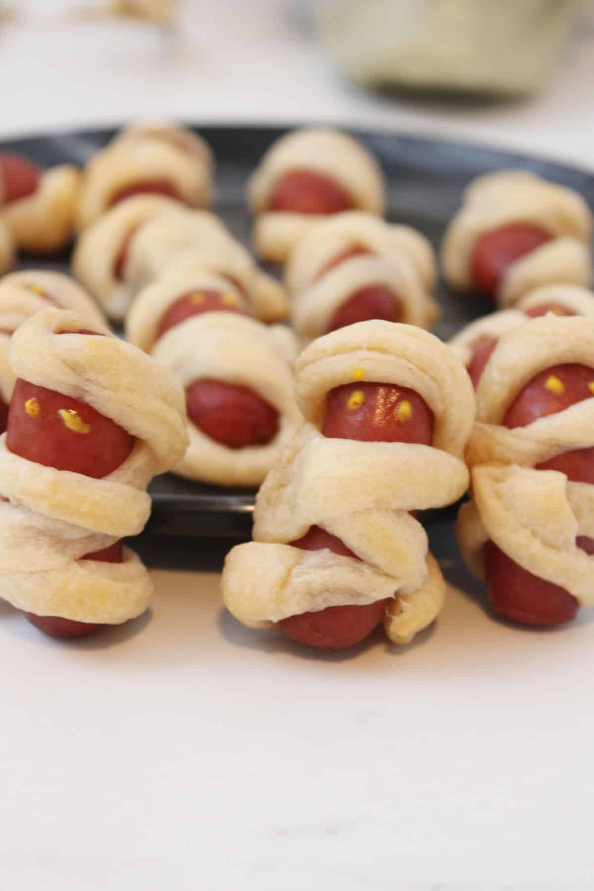 crescent roll mini mummy pigs in a blanket on a plate.