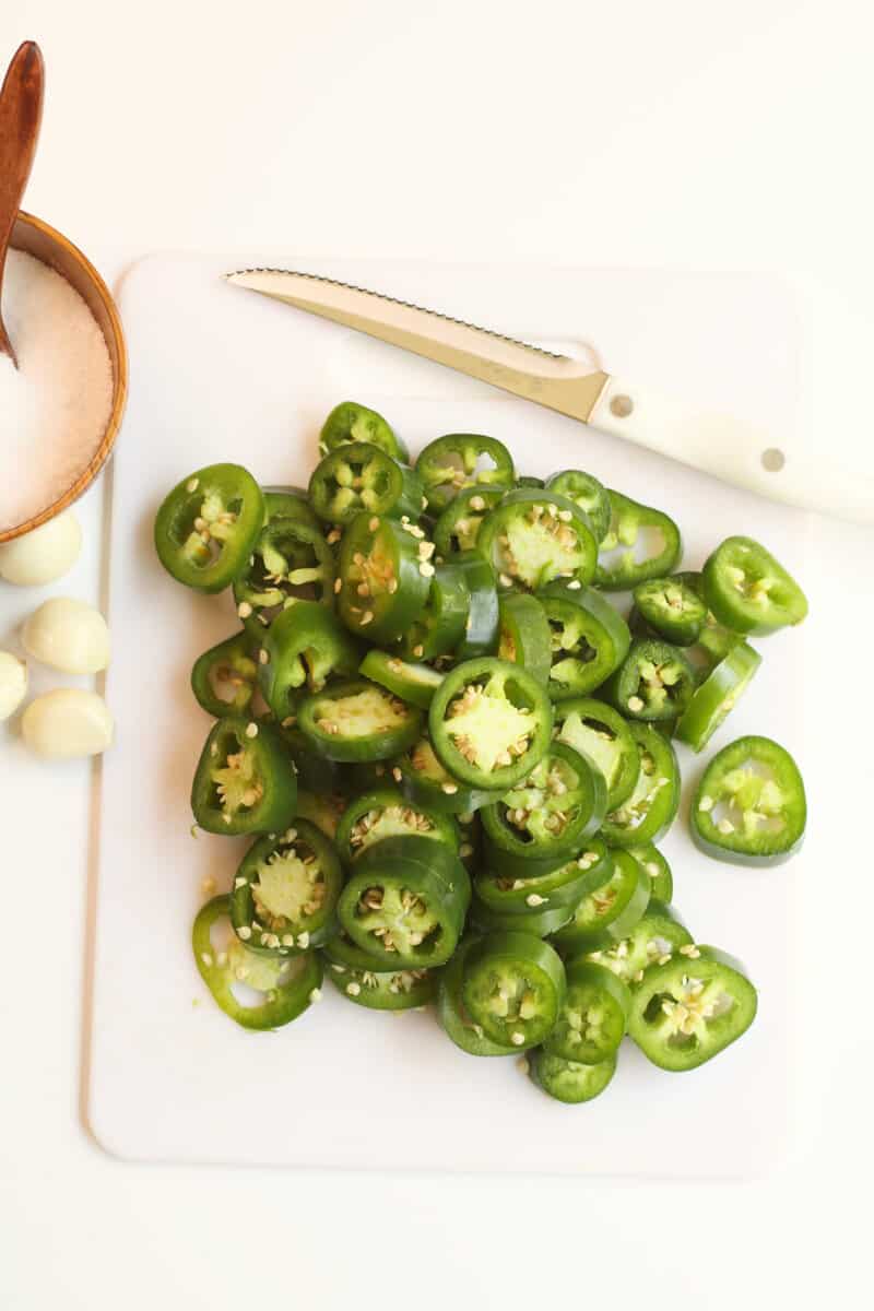 sliced jalapenos on a white cutting board.