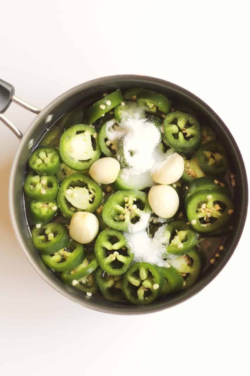 fresh sliced jalapenos and garlic with salt in a stainless steel pot.