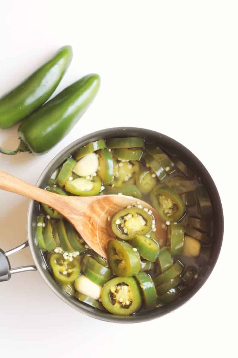 simmering jalapenos in a stainless steel pot.