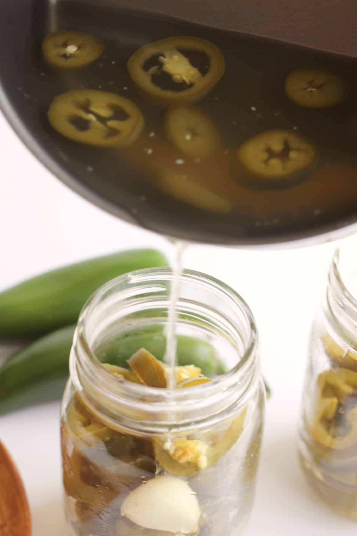 liquid being poured into a mason jar with garlic and sliced jalapenos.