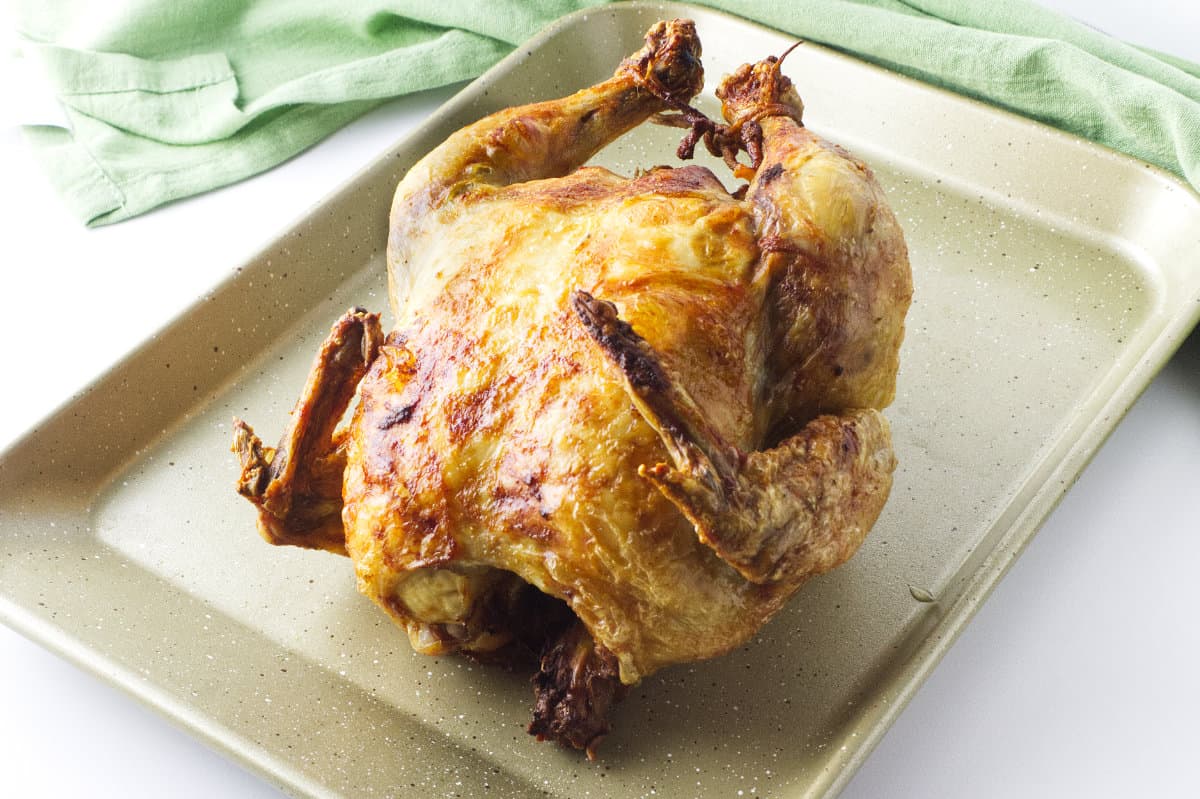 a golden brown rotisserie chicken off the spit resting on a baking tray