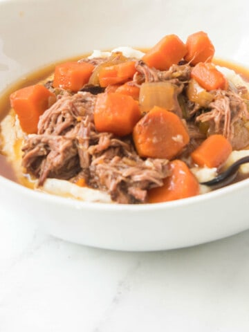 close up of bowl of pot roast and carrots on mashed potatoes.