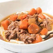 close up of bowl of pot roast and carrots on mashed potatoes.