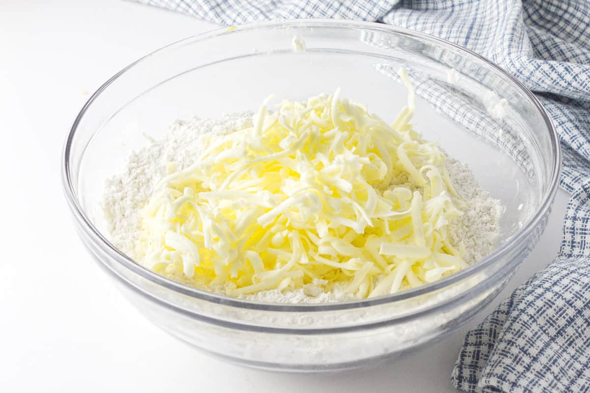 grated butter on top of dry scone ingredients in a clear glass bowl.