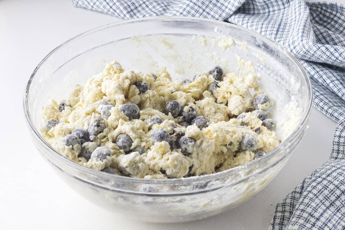 clear glass bowl of dough mixed with fresh blueberries.