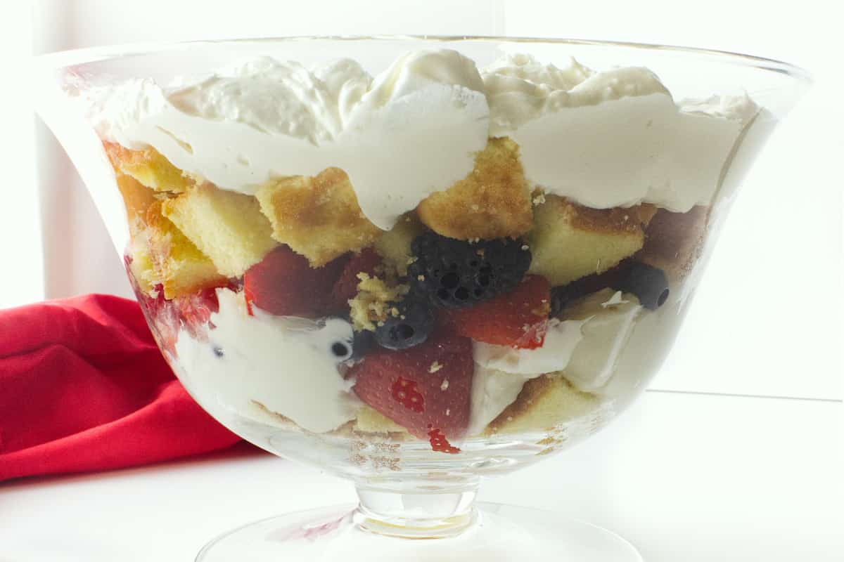 layers of cheesecake filling, pound cake, and assorted summer berries in a clear glass trifle bowl.