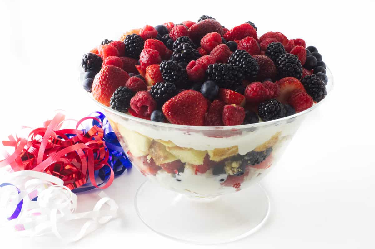 a large clear glass bowl filled layered with cake, berries, cheesecake, and more fruit on top.