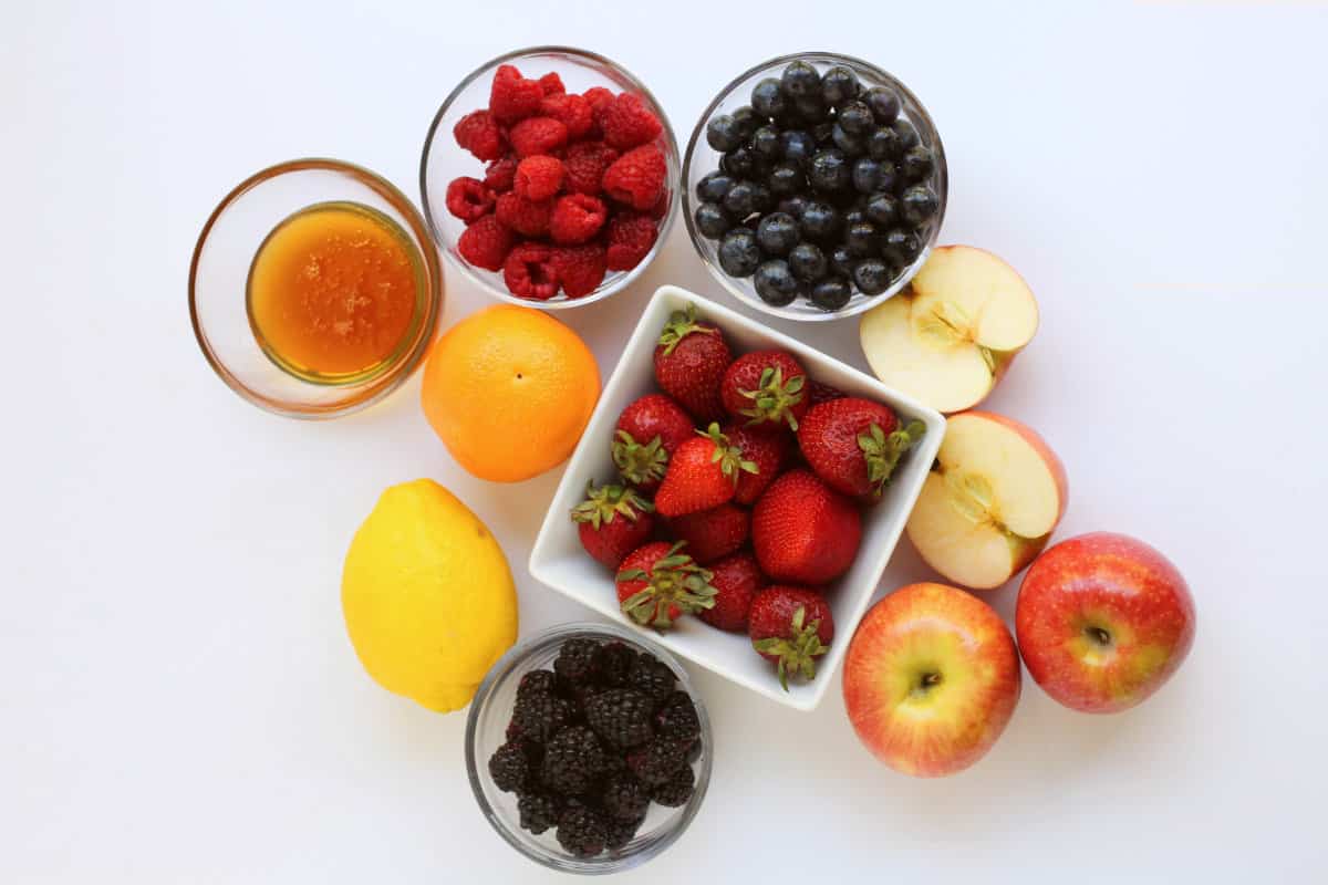bowls with honey, blackberries, strawberries, raspberries, strawberries and apples, oranges, and lemons.