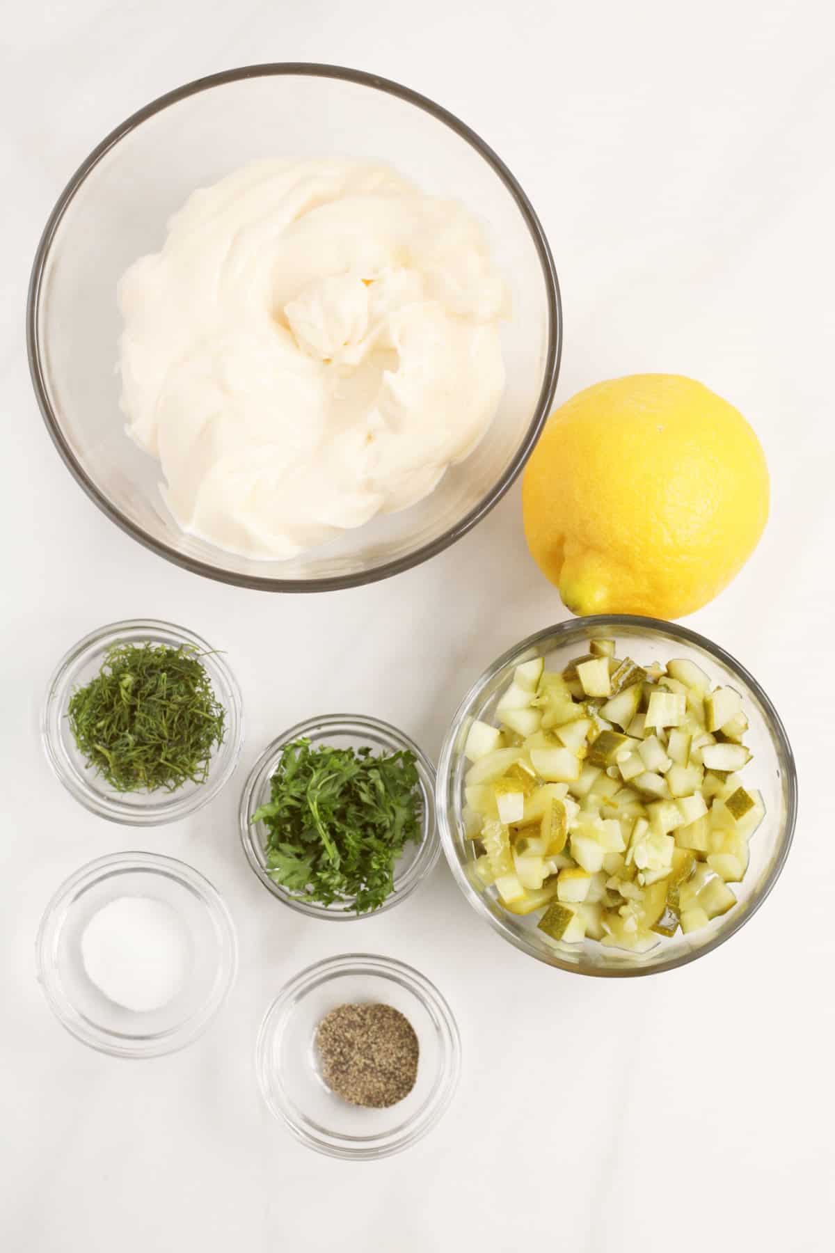 glass bowls with chopped dill pickle, chopped dill, chopped parsley, salt, pepper, lemon, and mayonnaise for making tartar sauce.