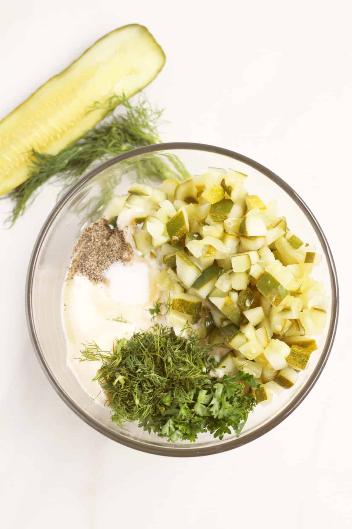 clear glass bowl with dill pickle, chopped dill, mayonnaise, and seasonings to mix together.