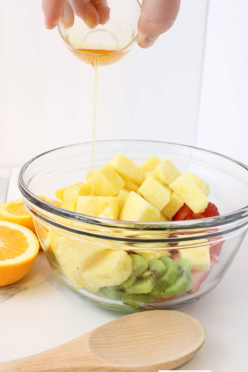 honey dressing drizzling into bowl of sliced fruits.