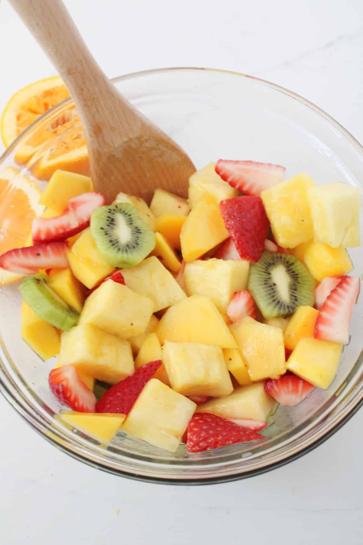 mixing dressing into bowl of sliced tropiccal fruit.