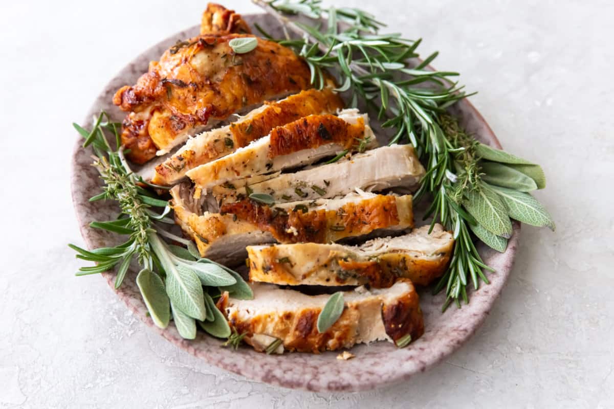 sliced turkey breast on a platter strewn with fresh sage and rosemary.