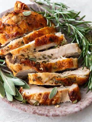 sliced turkey on a platter with herbs.