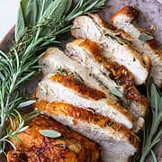 roast turkey breast sliced on a platter with herbs.