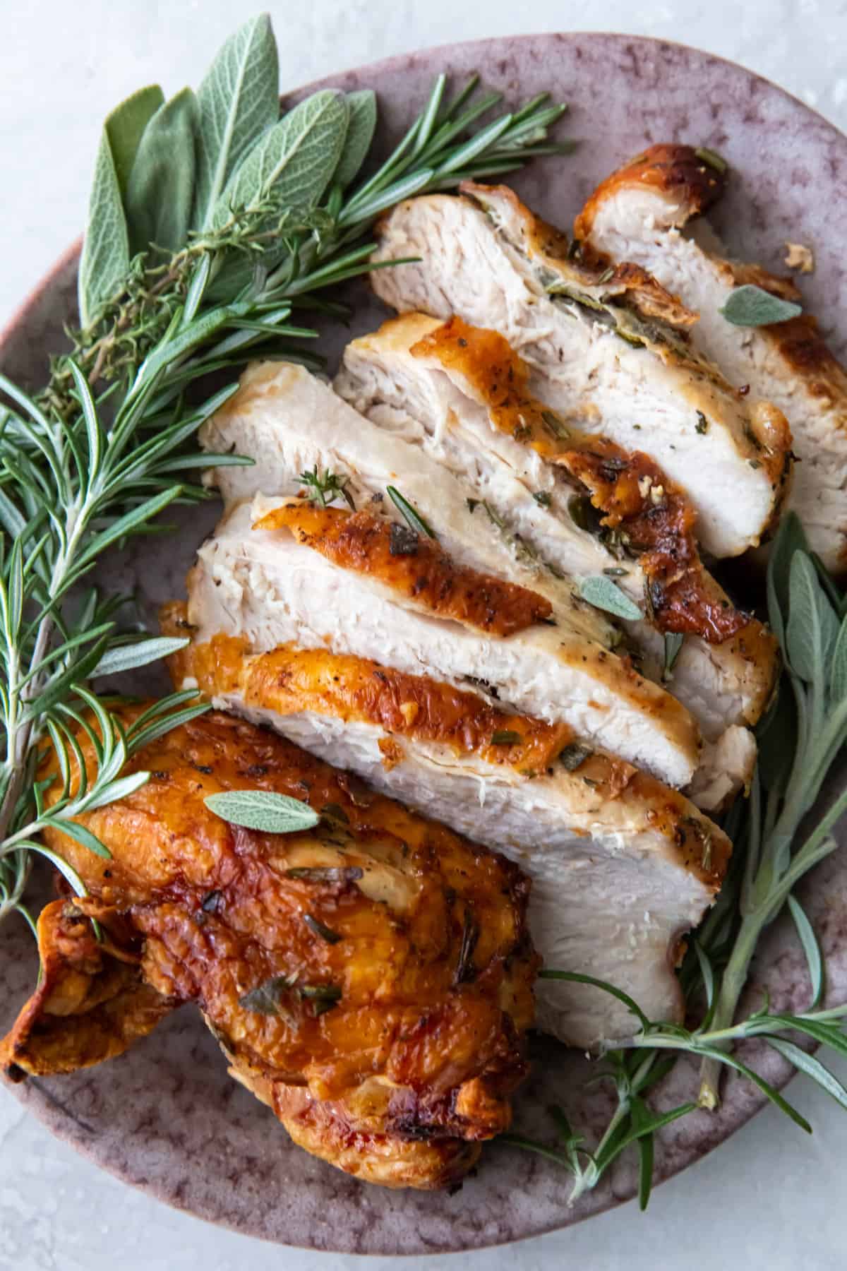 sliced air fried turkey breast on a platter with herbs.