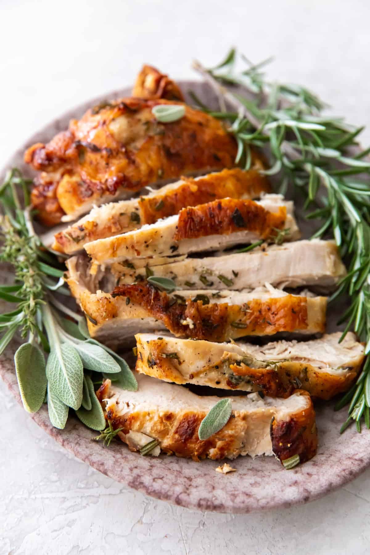roast turkey breast sliced on a platter with herbs.