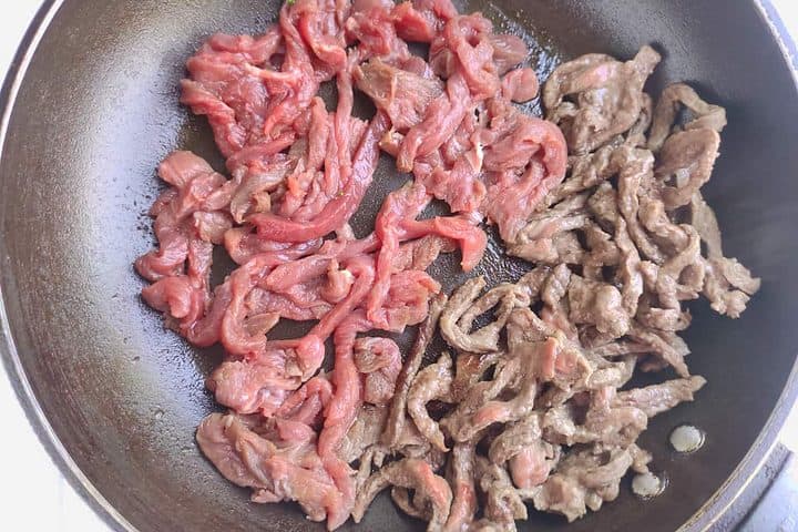 beef strips cooking in a skillet.
