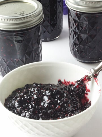 bowl of blackberry jam with three ball canning jars of jam in background.