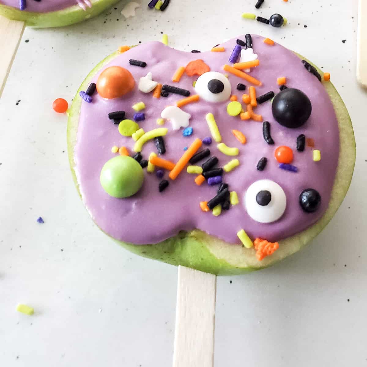 close up of purple candy apple slice with halloween sprinkles.