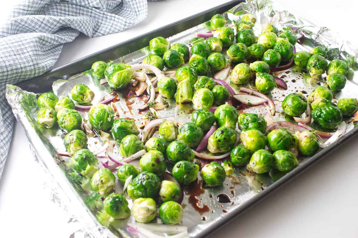 uncooked brussels sprouts spread out on a baking sheet with seasoning.